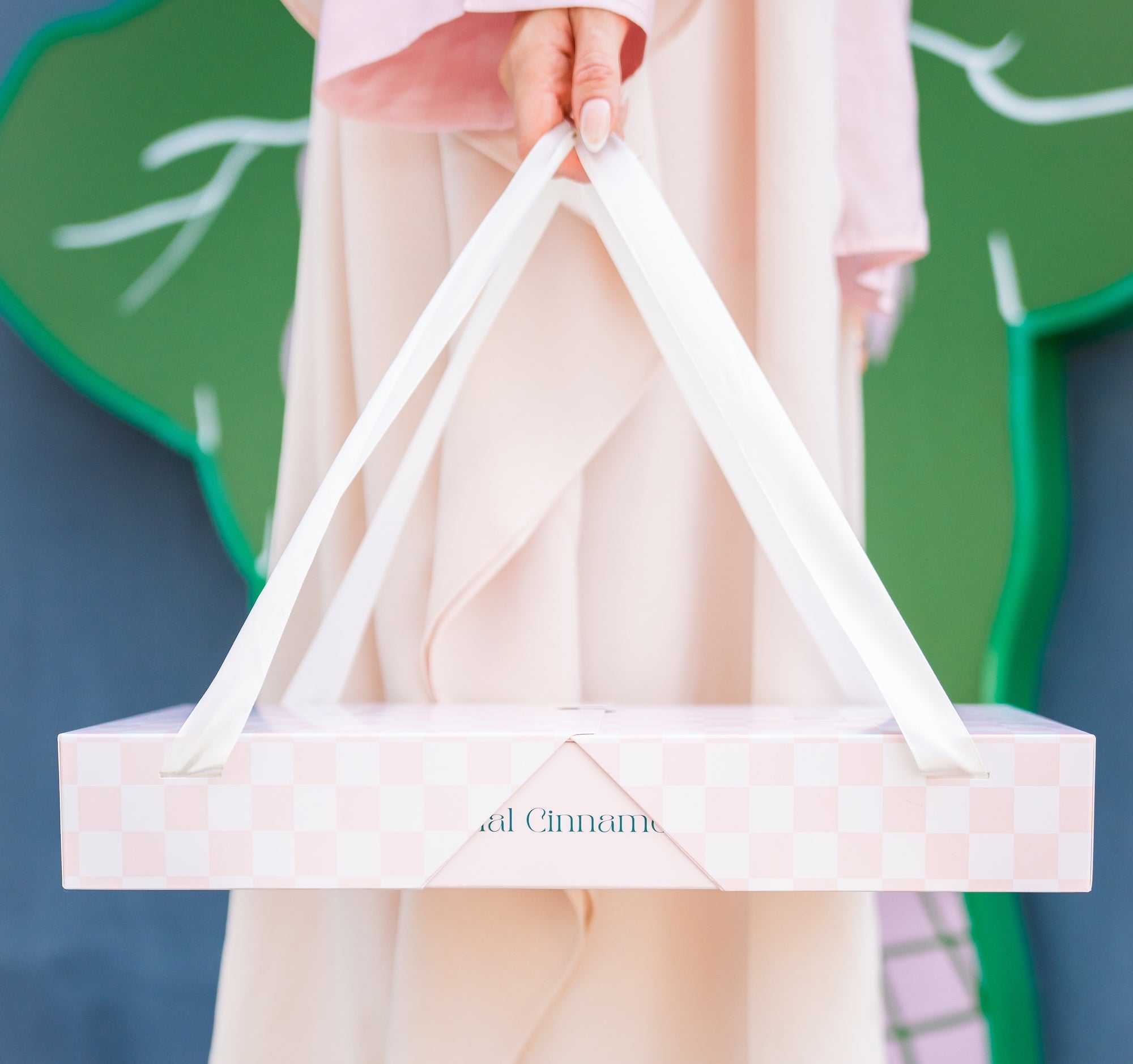 Person holding a CINNAMORE catering box against a green and blue background