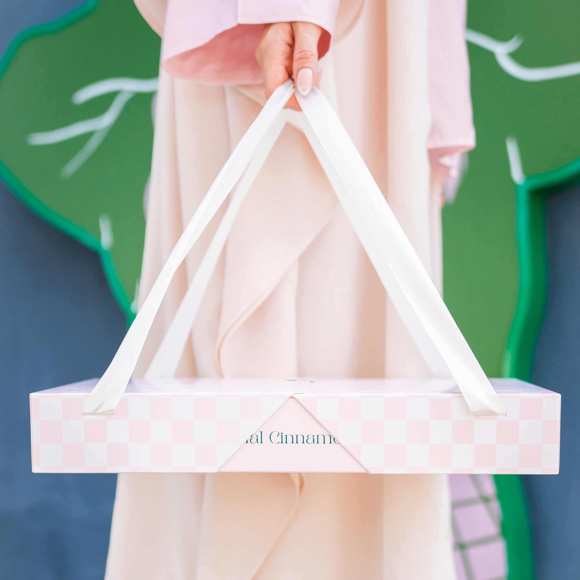Person holding a CINNAMORE catering box against a green and blue background