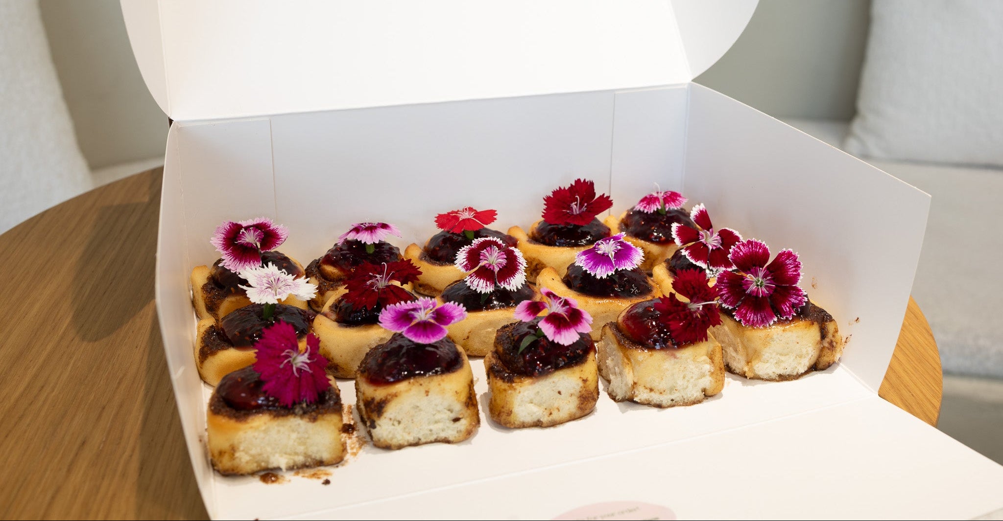 Box of small vegan cinnamon rolls with floral decorations on a wooden table.