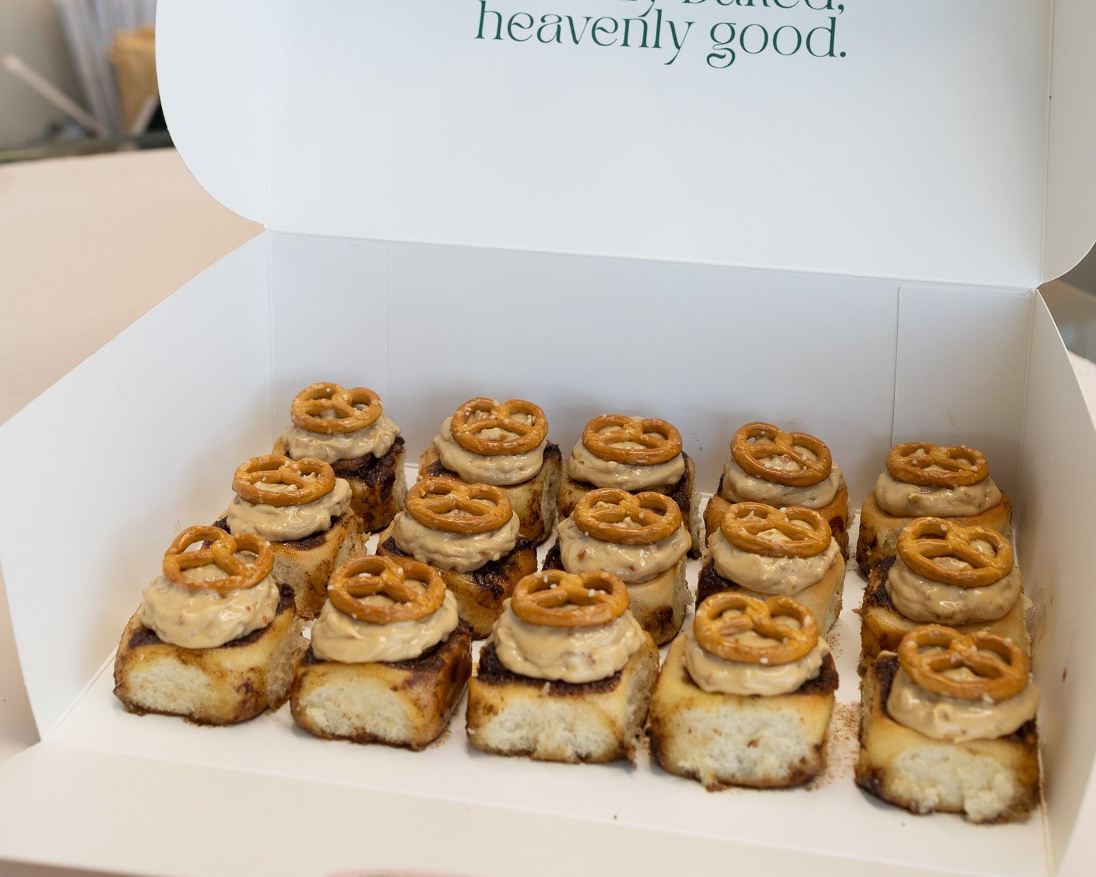 Box of pretzel cinnamon rolls with 'Freshly baked, heavenly good' text in a store setting.